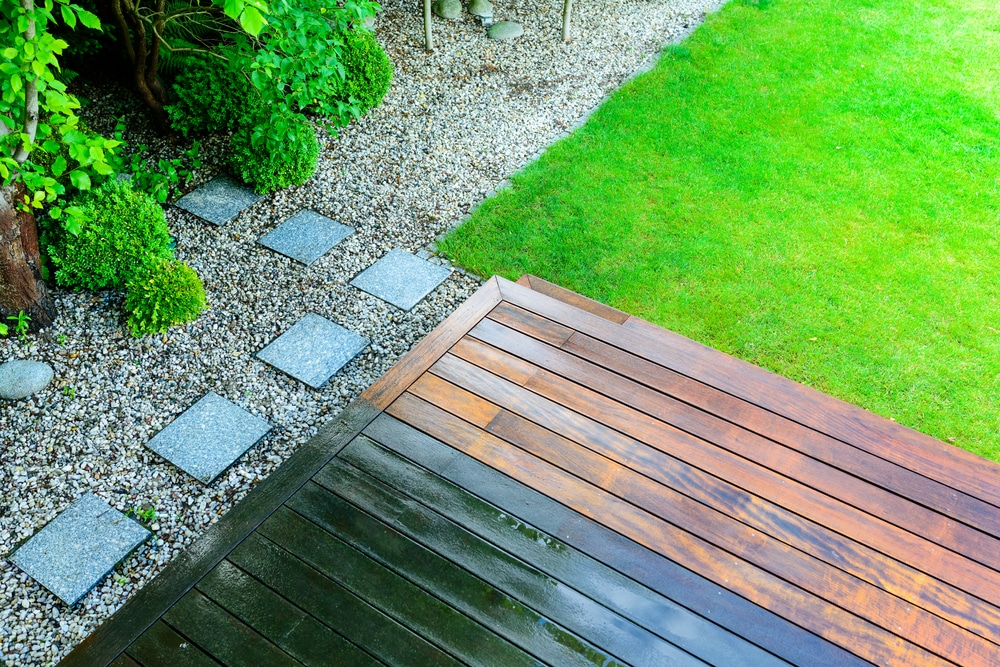 Wooden deck leading to a garden with a gravel path and stepping stones. Lush green grass and bushes line the path, creating a serene outdoor space. Enhance its beauty with the best window cleaning service in Northeast Kentucky for sparkling clarity that complements nature's charm.