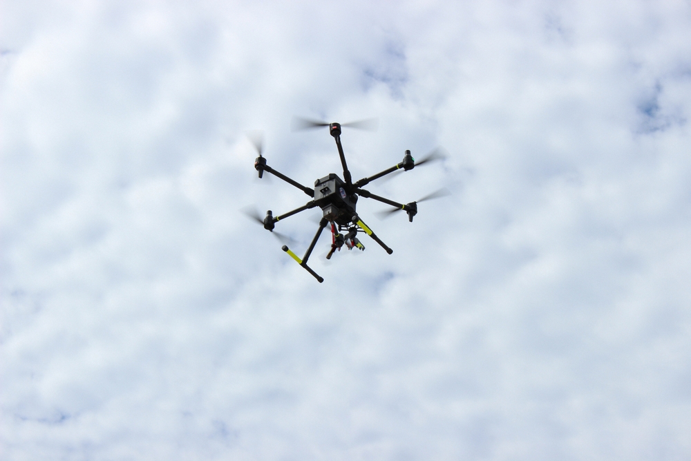 A drone with six propellers flies against a cloudy sky, resembling the precision of a pressure washing service in Fayette County, KY.